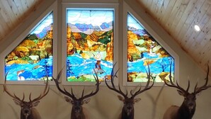 A room with wooden ceiling, four mounted deer heads, and three stained glass windows depicting landscapes. - August Just Opened Up & Beautifully Wild has A/C! 21-Z3031 (Bellvue)