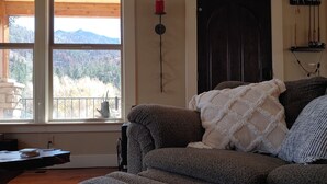 A cozy living room with a large window, a dark wooden door, and a fireplace. - August Just Opened Up & Beautifully Wild has A/C! 21-Z3031 (Bellvue)