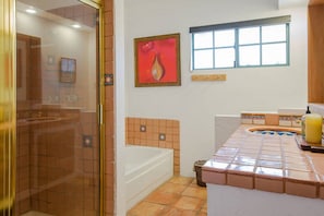 Ein Badezimmer mit Duschkabine aus Glas, einer Badewanne, einem Fenster und einer gefliesten Waschtischfläche.