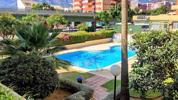Ein Swimmingpool, umgeben von Grünflächen, mit Blick auf einen Berg und Gebäude im Hintergrund.