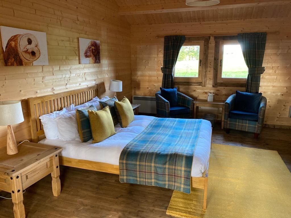 A wooden cabin room with a bed, two chairs, a table, and artwork on the wall.