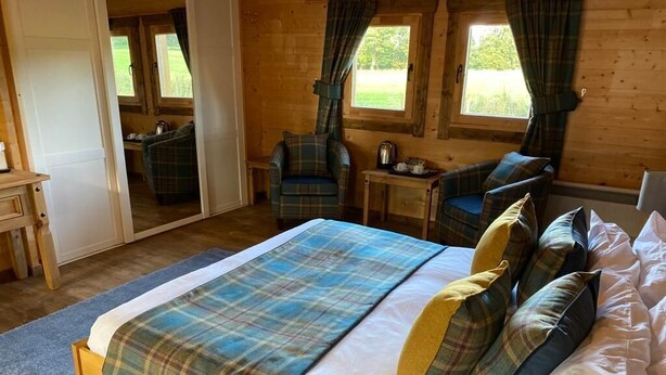 A wooden cabin bedroom with a bed, two chairs, a small table, and a mirror. - Shieldhill Castle Hotel (Biggar)