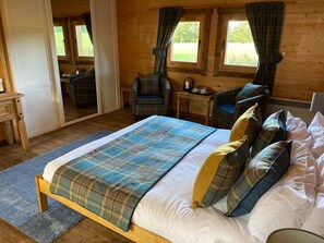 A wooden cabin bedroom with a bed, two chairs, a small table, and a mirror. - Shieldhill Castle Hotel (Biggar)