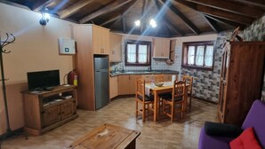 Une cuisine chaleureuse avec des meubles de rangement en bois, une table à manger avec des chaises, un canapé violet et un téléviseur posé sur un meuble en bois.