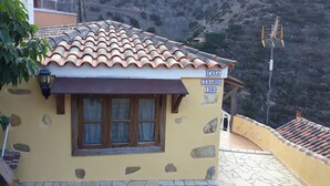 Un bâtiment jaune avec un toit recouvert de tuiles, une fenêtre avec des rideaux et une base en pierre.