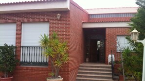 Un bâtiment en briques rouges avec une porte de garage blanche, un pot de fleurs et un escalier menant à l’entrée.