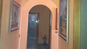 Un couloir doté d’un sol à carreaux, des œuvres d’art encadrées accrochées aux murs et une porte en arc donnant sur une autre pièce.