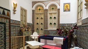 Ein traditionell eingerichteter marokkanischer Raum mit Badewanne, kleinem Tisch, Stuhl und einer Wand mit aufwendigen Kacheln.
