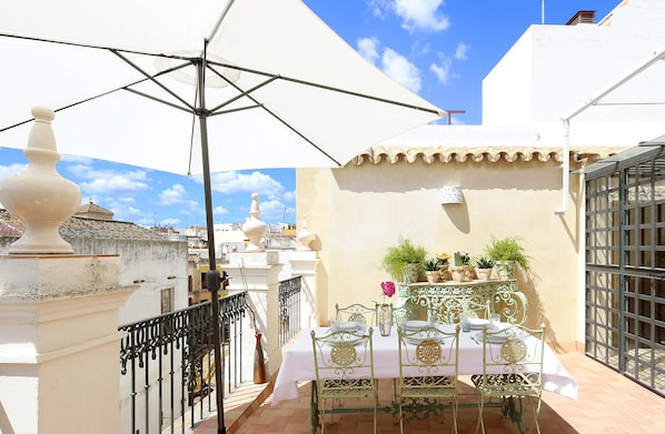 Una terraza con una mesa lista para comer, una silla de metal decorativa y una planta en maceta.