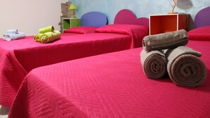 Een hotelkamer met twee bedden, elk met een rode sprei en kussens. Op de bedden liggen opgerolde handdoeken en er staat een lamp op een nachtkastje.