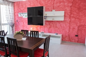 Un comedor con una mesa y sillas de madera, un televisor montado en la pared y un armario blanco con objetos decorativos.