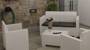 Een terras met rieten meubels, een stenen muur en een kast.