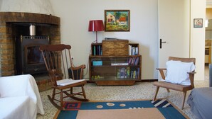 Una sala de estar acogedora con chimenea, un sillón mecedor, una estantería y una puerta que da a otra habitación.