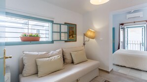 A cozy room with a sofa, a window with a view, a wall-mounted lamp, and a door leading to another room. - IN OFFER - LUXURY HOUSE WITH TERRACE IN LA JUDERIA, PAX 10 (SEVILLA)