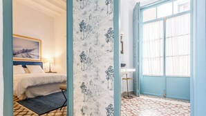 A bedroom with a bed, a nightstand, a lamp, a window with curtains, and a patterned wall. - IN OFFER - LUXURY HOUSE WITH TERRACE IN LA JUDERIA, PAX 10 (SEVILLA)