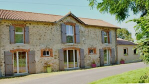 A two-story stone house with a tiled roof, multiple windows with shutters, and a paved driveway. - Gîte with Jacuzzi in the countryside 18 kms from the ocean (La Boissière-Des-Landes)