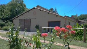A building with a brick facade, a garage door, and a garden with pink flowers. - Gîte with Jacuzzi in the countryside 18 kms from the ocean (La Boissière-Des-Landes)