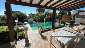 Un espace extérieur abrité comprenant une piscine, des chaises longues et une table.