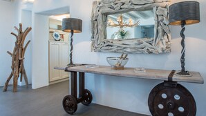 Ein modernes Interieur mit rustikalem Dekor, das einen Holztisch auf Rollen, zwei Lampen und einen einzigartigen Spiegel mit Steinrahmen zeigt.