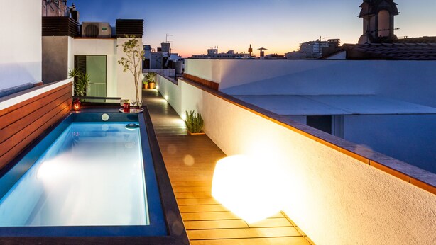 A rooftop pool with wooden decking and a view of the city skyline at dusk. - Exclusive house in Sitges center with pool and terraces, steps from beach (Sitges)