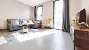 A modern living room with a grey sofa, a round coffee table, a wicker chair, and a TV on a wooden cabinet. - Exclusive house in Sitges center with pool and terraces, steps from beach (Sitges)