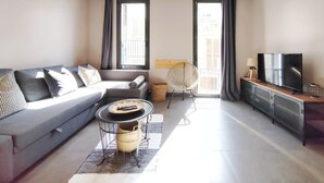 A modern living room with a grey sofa, a round coffee table, a wicker chair, and a TV on a cabinet. - Exclusive house in Sitges center with pool and terraces, steps from beach (Sitges)
