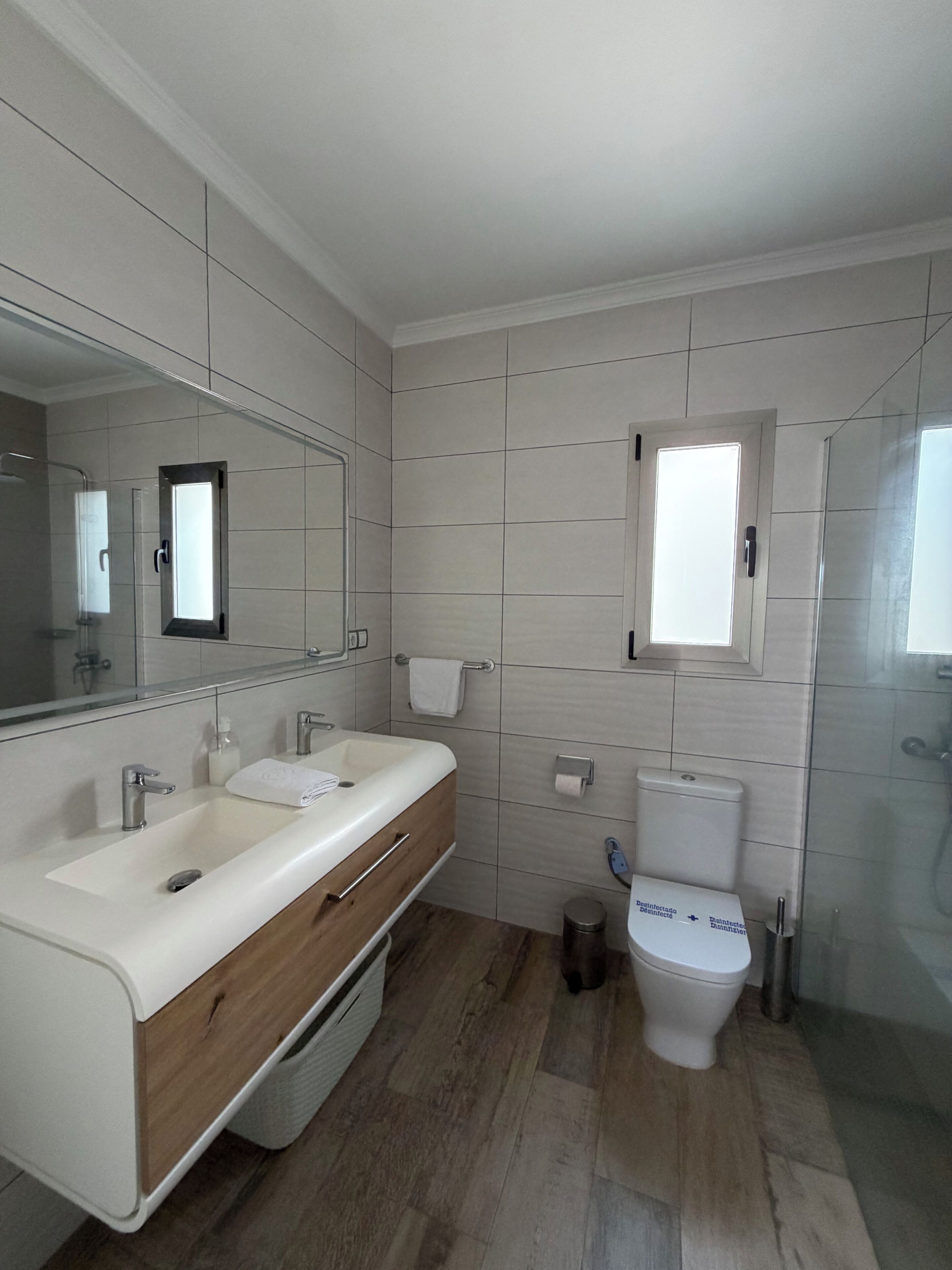 Une salle de bain comprenant un meuble-lavabo à deux vasques, des toilettes, un espace douche et un miroir.