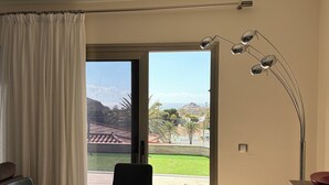 A room with a dining table, chairs, a desk with a computer, a lamp, and a sliding glass door leading to a patio with a view of a mountain and a cityscape. - House / Villa - Tauro - Mogán (Mogan)