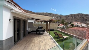 A modern outdoor patio with a barbecue, seating area, and a view of a hillside. - House / Villa - Tauro - Mogán (Mogan)