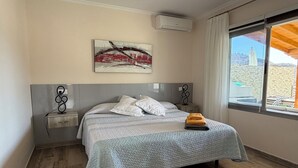 A bedroom with a bed, a painting, an air conditioner, a window with curtains, and a view of the outside. - House / Villa - Tauro - Mogán (Mogan)