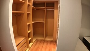 Un vestidor amplio con varias estanterías y cajones, suelo de madera y una lámpara en el techo.
