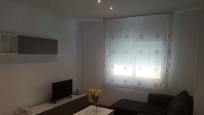 Una sala de estar moderna con un televisor de pantalla plana, una mesa de centro blanca, un sofá y un ventanal con cortinas.