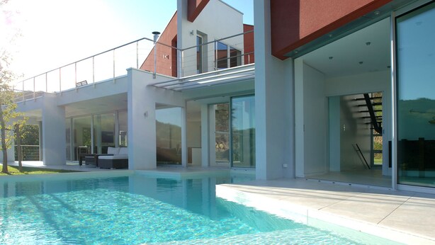 A modern house with a swimming pool, large glass doors, and a balcony.