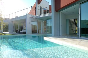 A modern house with a swimming pool, large glass doors, and a balcony.