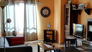 Una sala de estar con un sofá, una mesa de comedor, un televisor y un reloj en la pared.