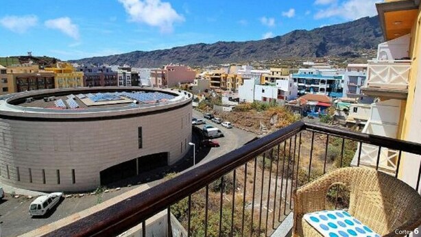 Un balcón con vistas a un paisaje urbano, que incluye edificios y una montaña al fondo.