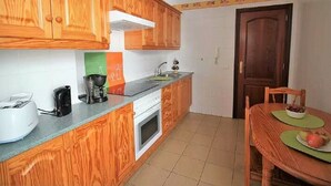 Una cocina compacta con armarios de madera, horno integrado y un comedor con mesa y sillas.