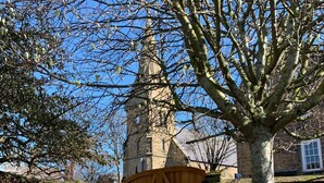 A stone wall with a wooden gate, a tree, and a building with a tower in the background. - Fossil Bank, a luxury detached retreat in the heart of Alnmouth, with parking (Alnmouth)