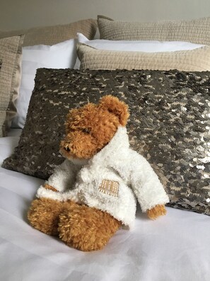 A plush teddy bear sitting on a bed with a white pillow and a sequined pillow. - Fossil Bank, a luxury detached retreat in the heart of Alnmouth, with parking (Alnmouth)
