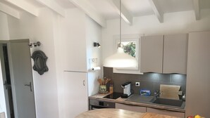 Ett modernt kök med ett träbord, en hängande taklampa och en skål med frukt på bänkskivan.