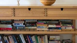 Een trap met een houten leuning, een aan de muur bevestigd horloge, een houten schaal en een boekenplank vol boeken.