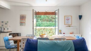 Een eetgedeelte met een houten tafel, blauwe stoelen en uitzicht op groen via een open deur.