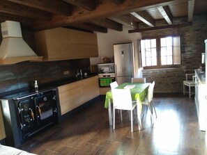 A kitchen with a stove, oven, and microwave. There is a dining table with chairs and a window with curtains.