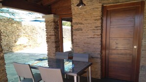 An outdoor dining area with a stone wall, a wooden door, and a glass table with chairs.