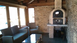 A cozy patio area with a stone fireplace, wicker furniture, and a view through large windows.