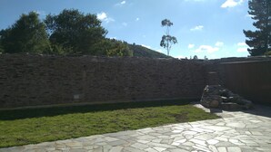 A stone wall, a stone patio, and a grassy area with trees in the background.