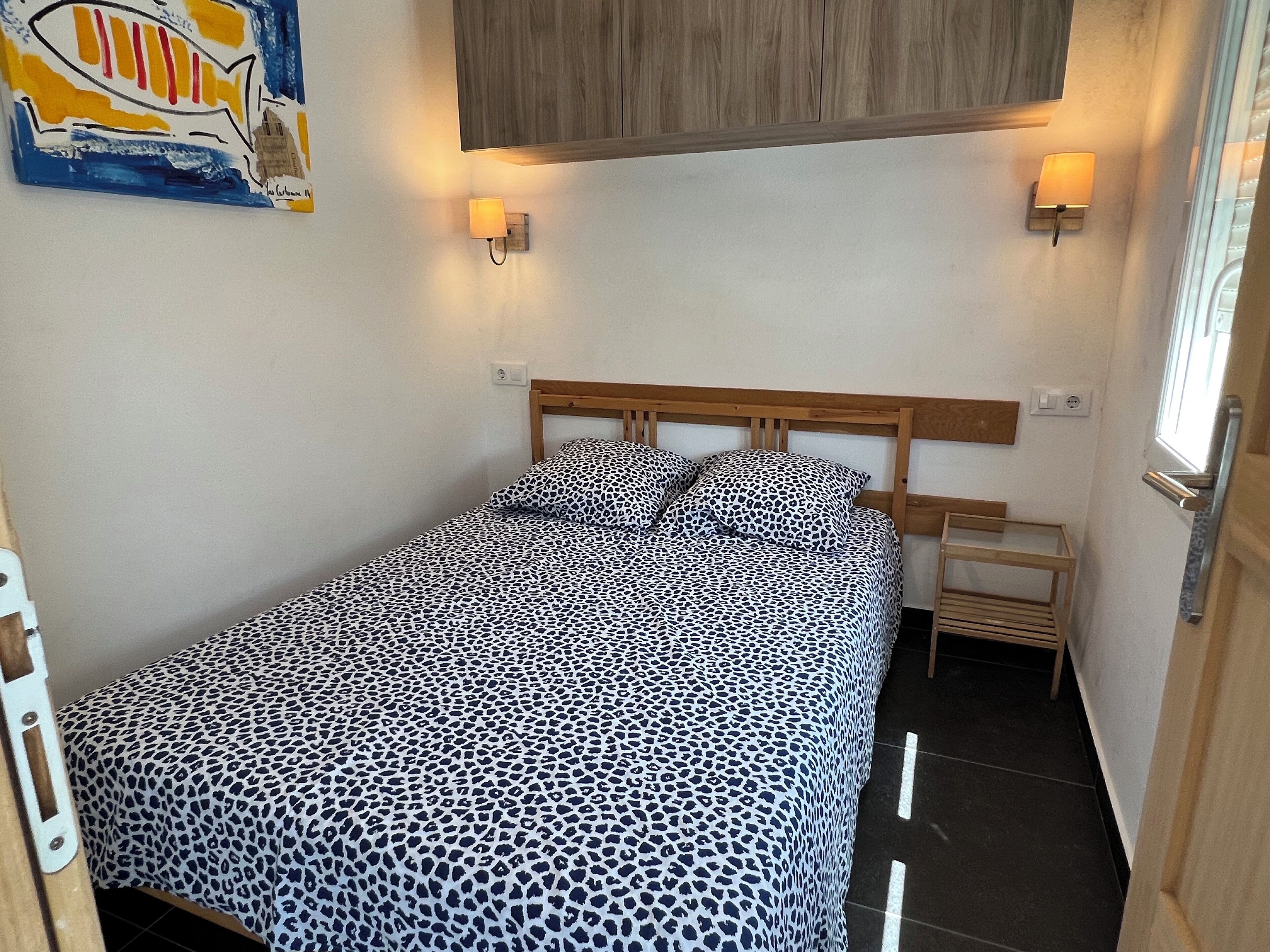 A small, neatly made bed with a leopard print bedspread, a wooden headboard, and two wall-mounted bedside lamps.