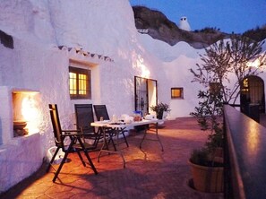 A cozy outdoor dining area with a table and chairs, surrounded by white walls and a tiled floor.