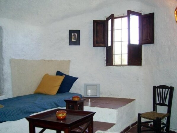 A small, cozy room with a bed, a chair, a table, and a window.