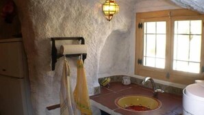A rustic kitchen with a stone wall, a wooden window, a sink, and a stove. - Troglodyte House Cueva Almendro, Granada Province (Free WiFi) (Guadix)